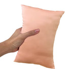 A hand holding a peach colored, mini-sized, travel pillow.