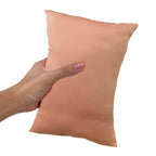 A hand holding a beige colored, mini-sized travel pillow.